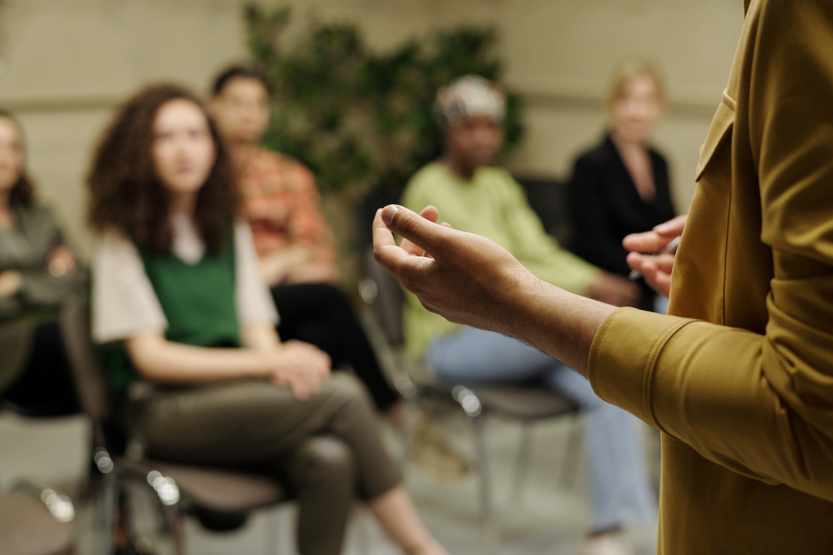 Hands of young business coach explaining information to group of employees at seminar while standing in front of audience