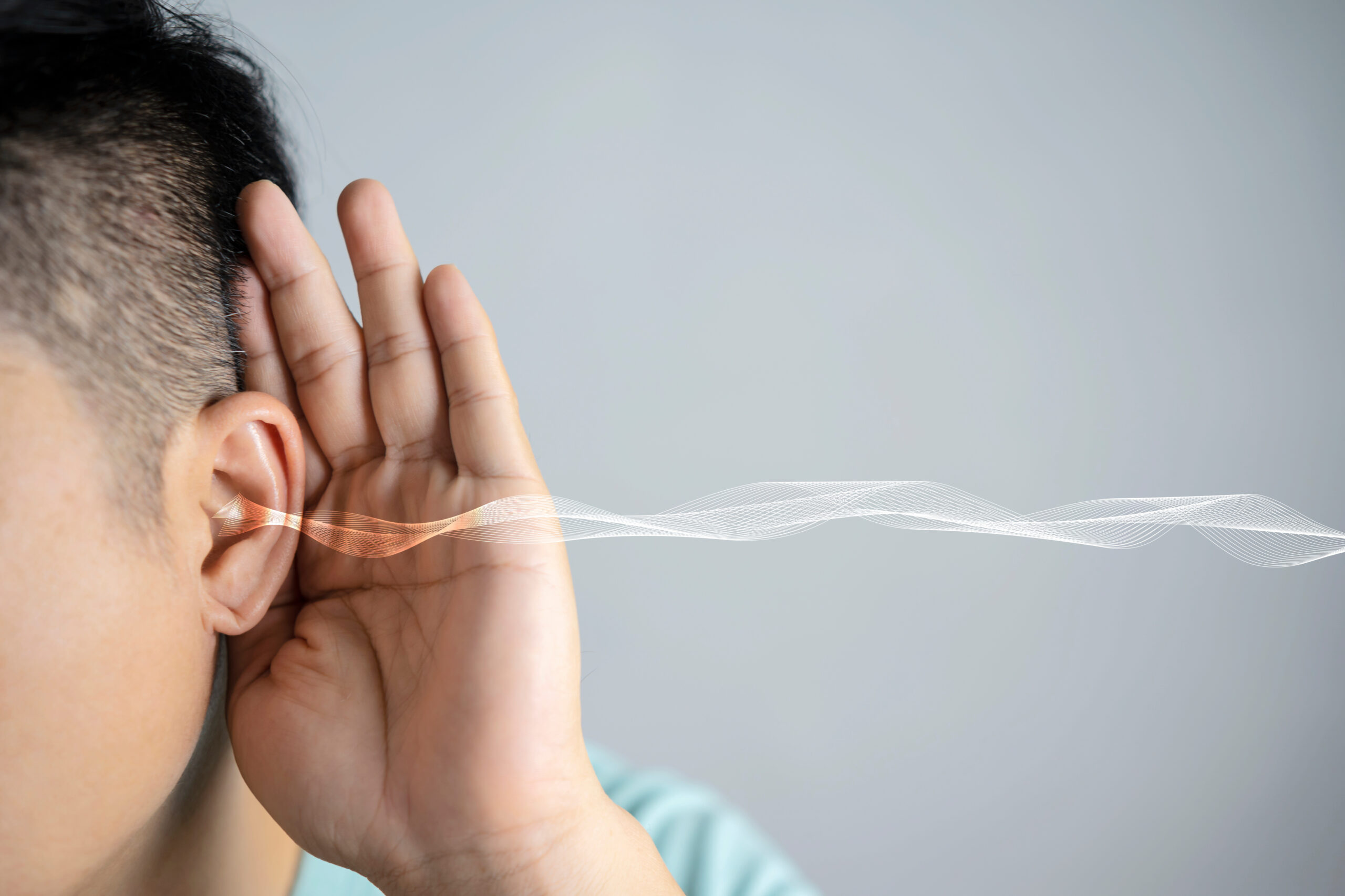 The man listens attentively with her palm to her ear close-up, a grey background